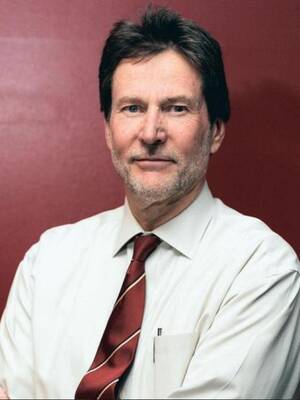 older man in a white shirt with a red tie looks into the camera with a red backgroup