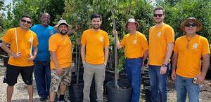 Group of men wearing yellow shirts smiling at the camera while holding a tree