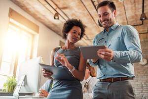 a woman and a man walk down the hall discussing something that they see on a tablet